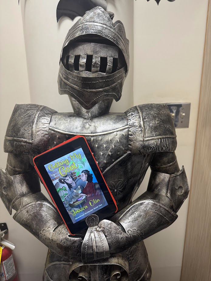 Getting My Goat, seen on the screen of an ereader, resting on the hands of a suit of armor.